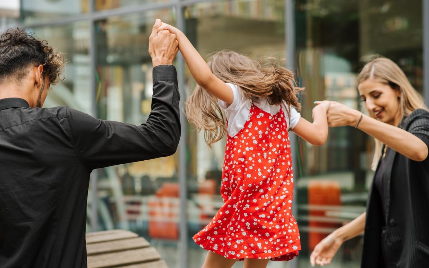 Parents holding their child's hands. The child is jumping
